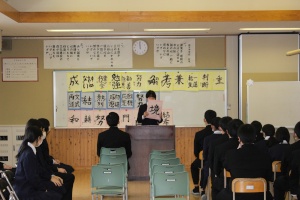 教室で一人の生徒が椅子に座っている沢山の生徒の前で正面に立って発表している写真