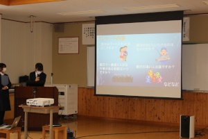 教室の正面に設置されたスクリーンに、資料を写しながら正面の壇上で発表している生徒の写真