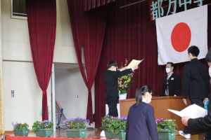 正面に日の丸が掲げられた体育館の壇上で卒業証書を授与されている男子生徒の写真
