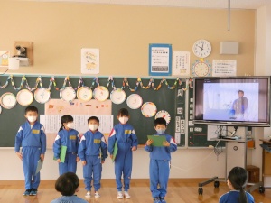 大きなモニターが設置された教室で、マスクをした5人の児童たちが発表をしている写真