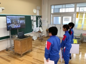 教室で大きなモニター越しにオンライン学習をしている3人の児童たちの写真