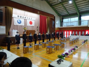 体育館で制服姿の卒業生がステージ前に横一列で整列している写真