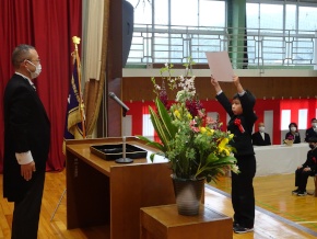 体育館のステージ上で燕尾服を着た校長先生から卒業証書を受け取っている男子児童の写真