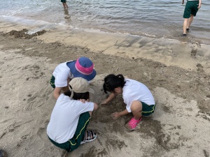 児童3人がしゃがんで頭を寄せ合って砂浜を見ている写真