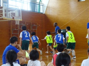 バスケットゴールの前で走る児童と長身の外国人の写真