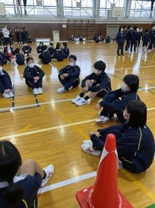 体育館で円になって体育座りをして話している生徒たちの写真