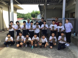 校舎の前で完成した木工作品を手に持つ児童たちの集合写真