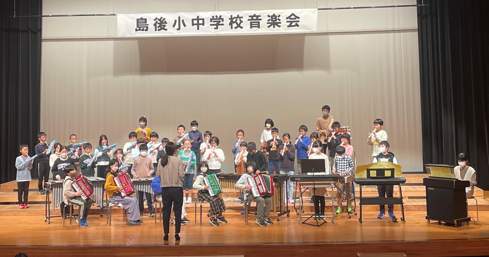 講堂で児童たちがアコーディオンや鍵盤ハーモニカを演奏している写真