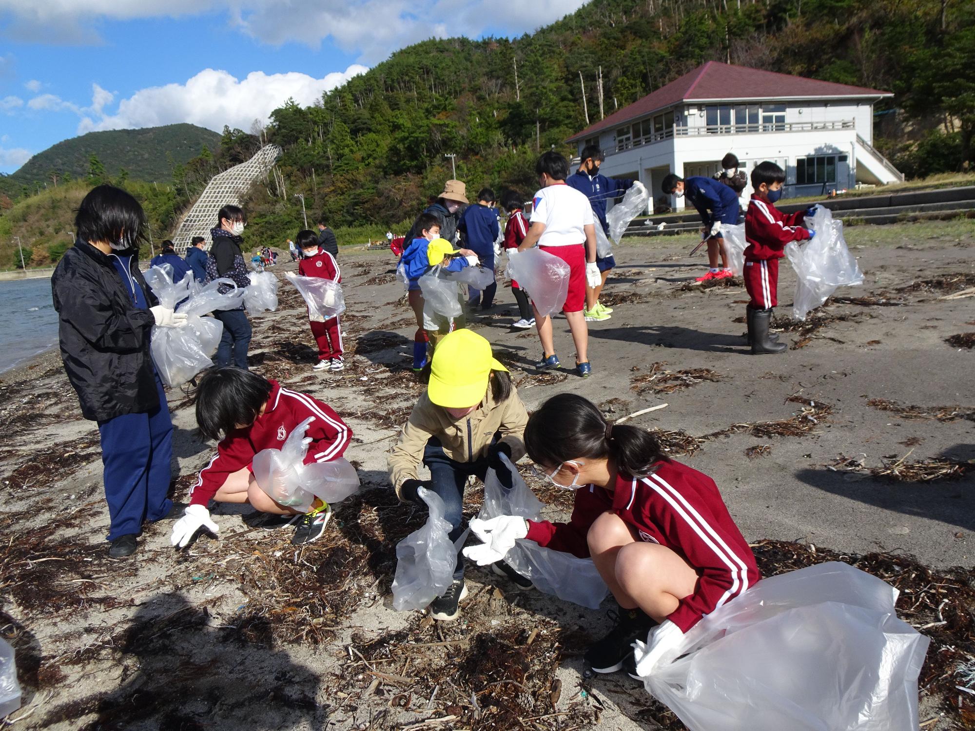 海辺でジャージ姿の子供たちがごみ拾いをしている写真