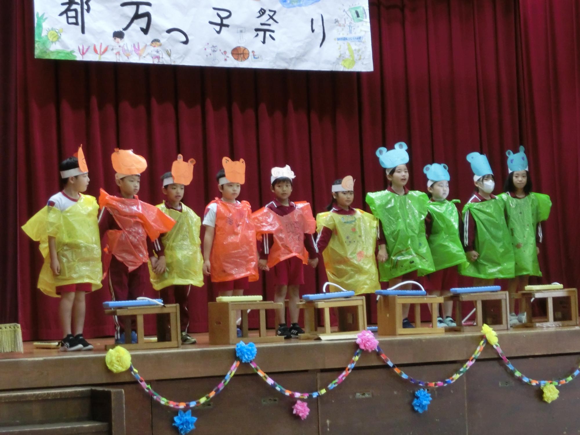 体育館の舞台で児童たちがカラフルな衣装を着て発表している写真