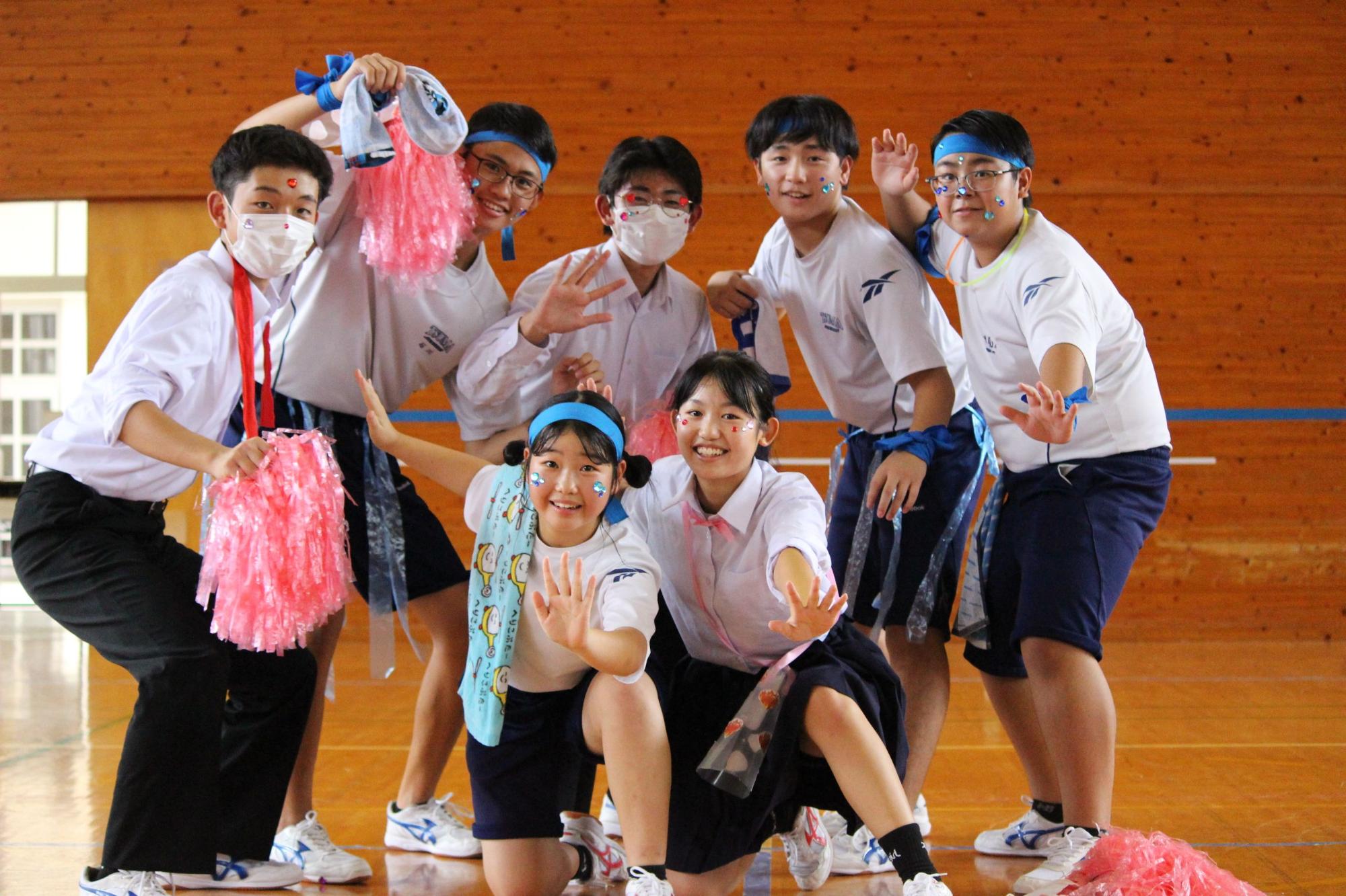 青いハチマキをつけピンクのボンボンを持った生徒たちが集合している写真