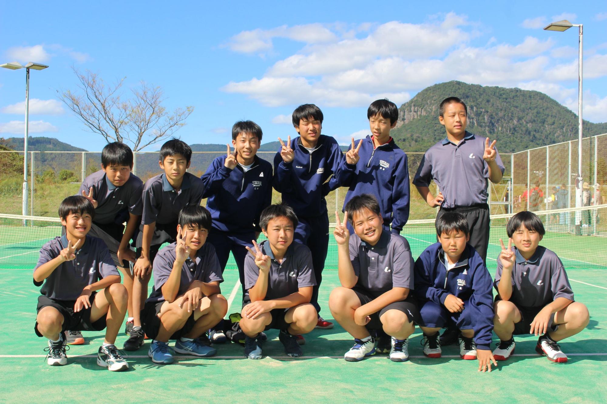 テニスコートで男子生徒が2列に並びピースをしている写真