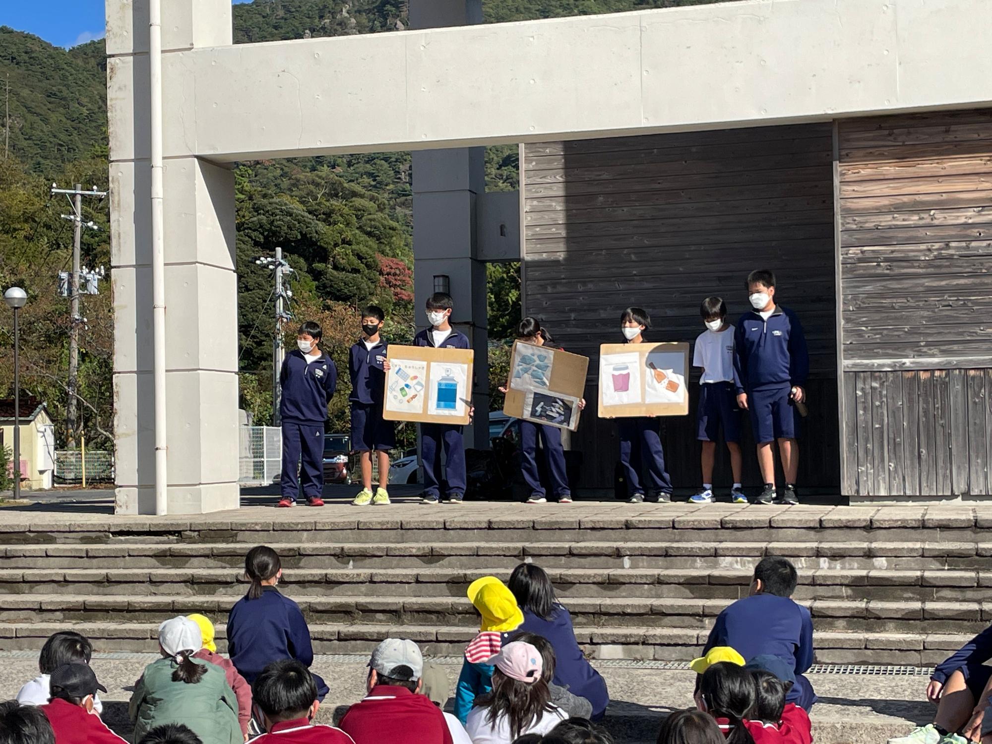 階段の上でボードを掲げる生徒たちと見上げる児童たちの写真