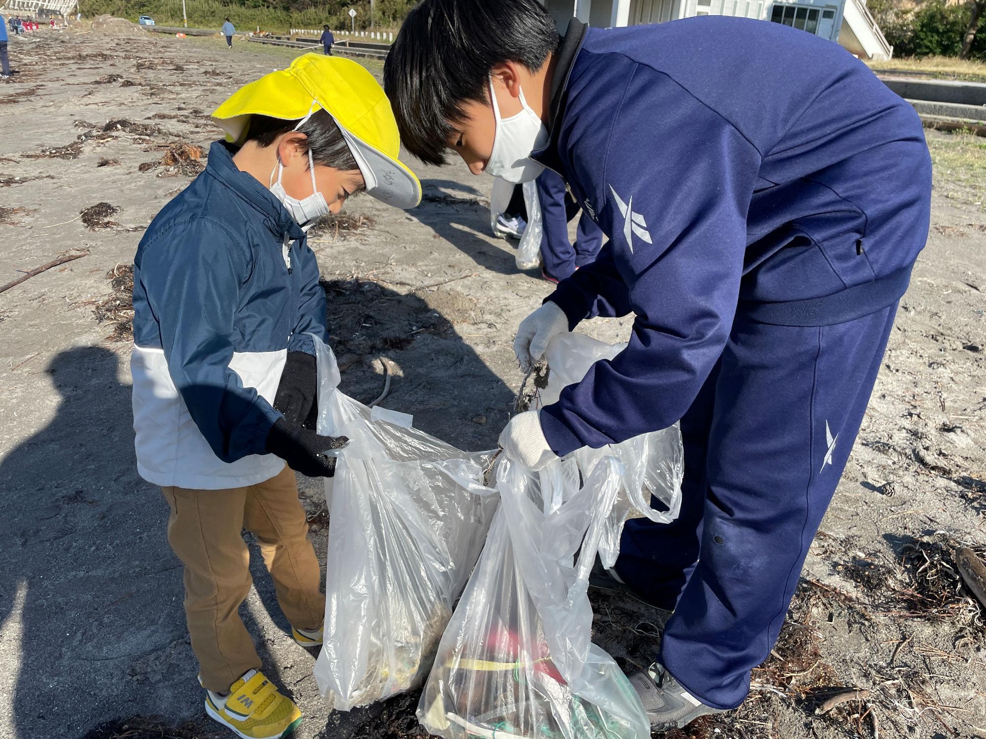 黄色い帽子をかぶった園児と生徒がゴミ拾いをしている写真