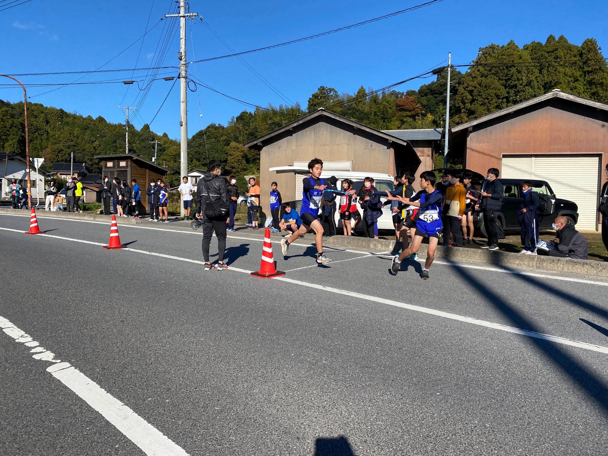 道路を走る生徒がバトンを渡そうとしている写真