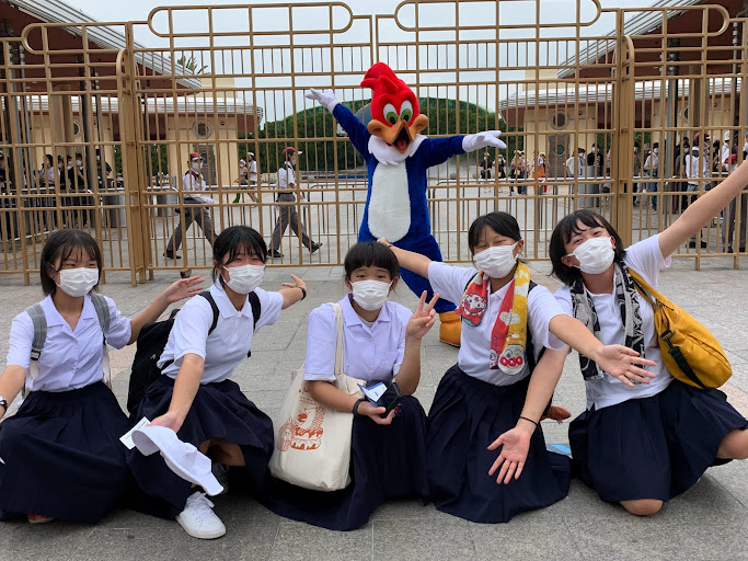 頭が赤い鳥のキャラクターの前に座り記念撮影をしている5人の女子生徒の写真