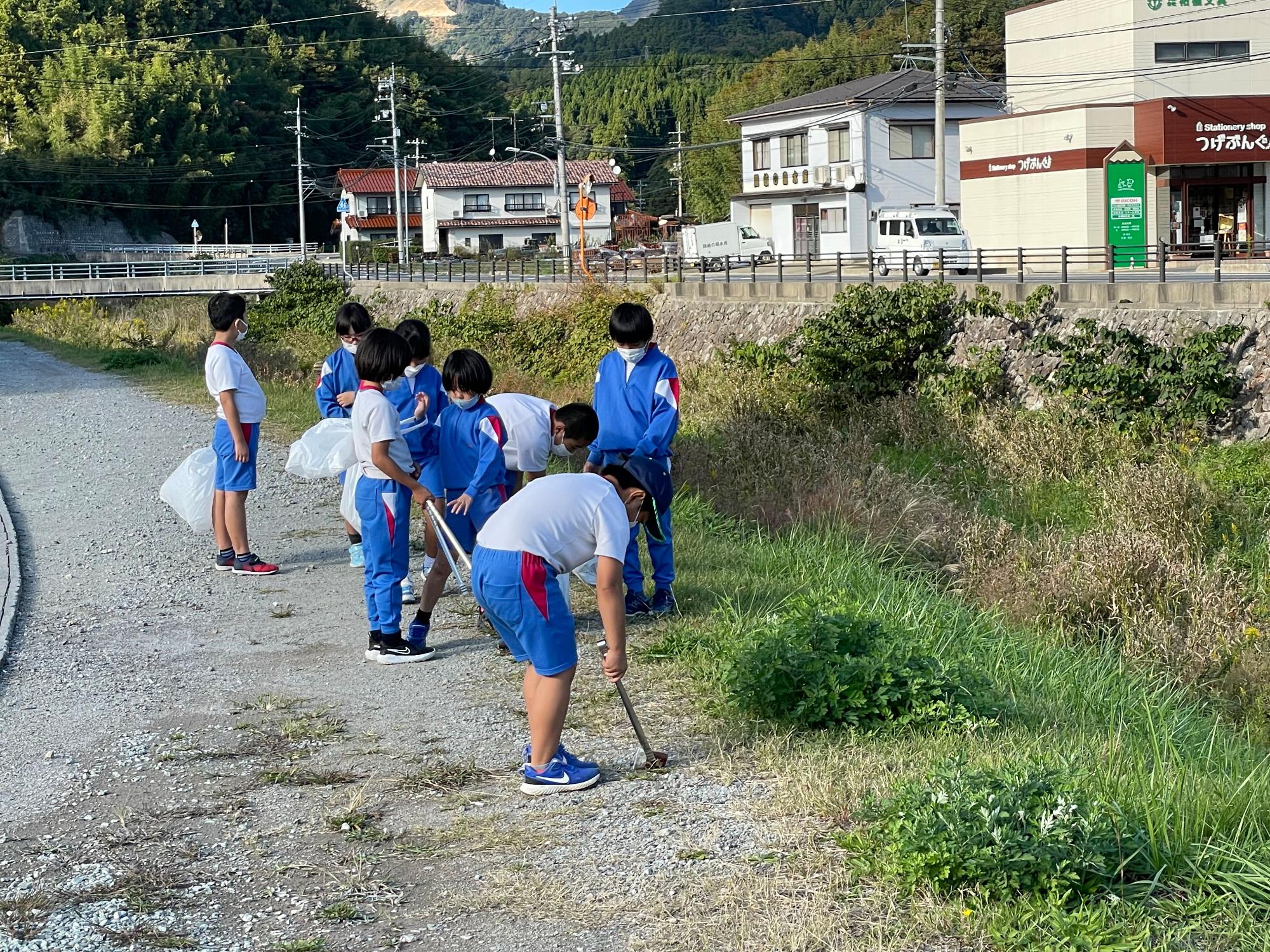 水路沿いの砂利道のごみを拾う児童たちの写真