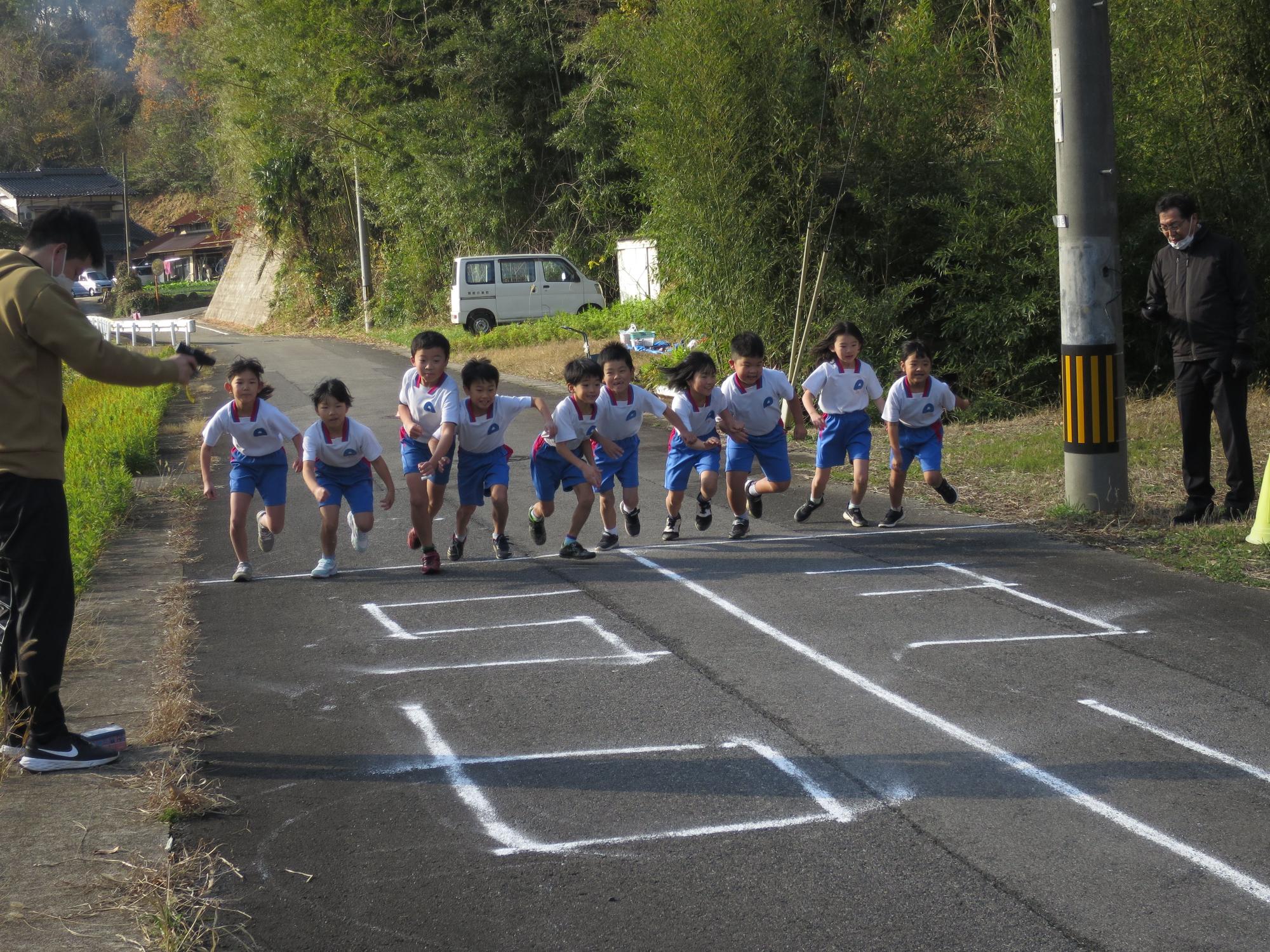 緑に囲まれた道路で一斉に駆け出す児童たちの写真