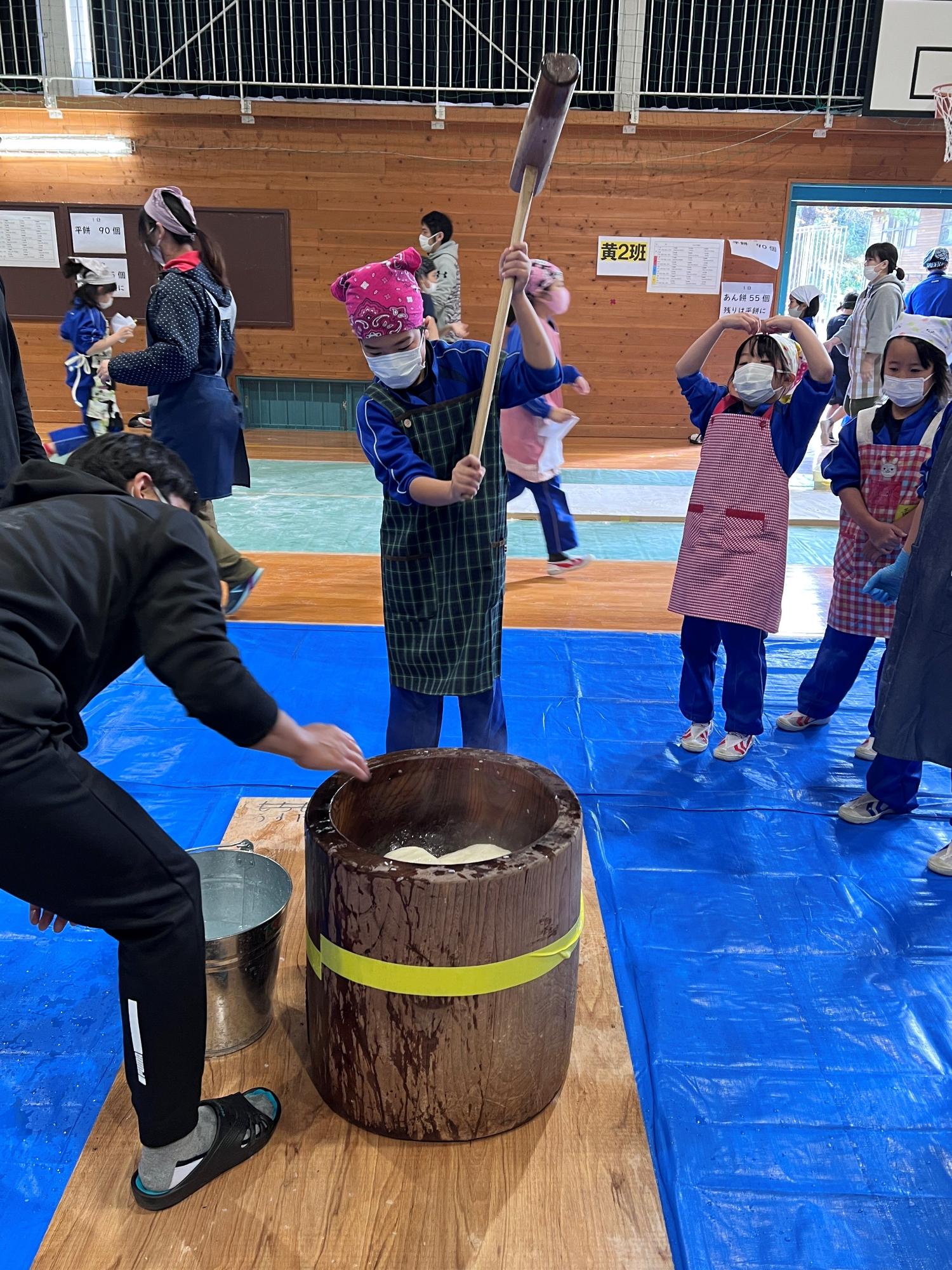 体育館で杵を振り上げて餅をつこうとしている男子児童の写真