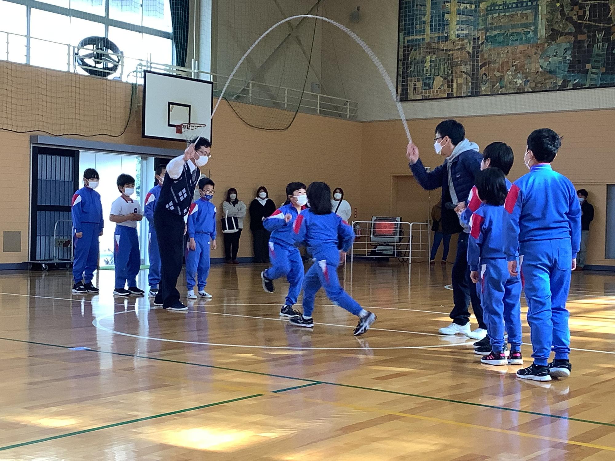 体育館で児童たちが先生と一緒に大縄跳びをしている写真