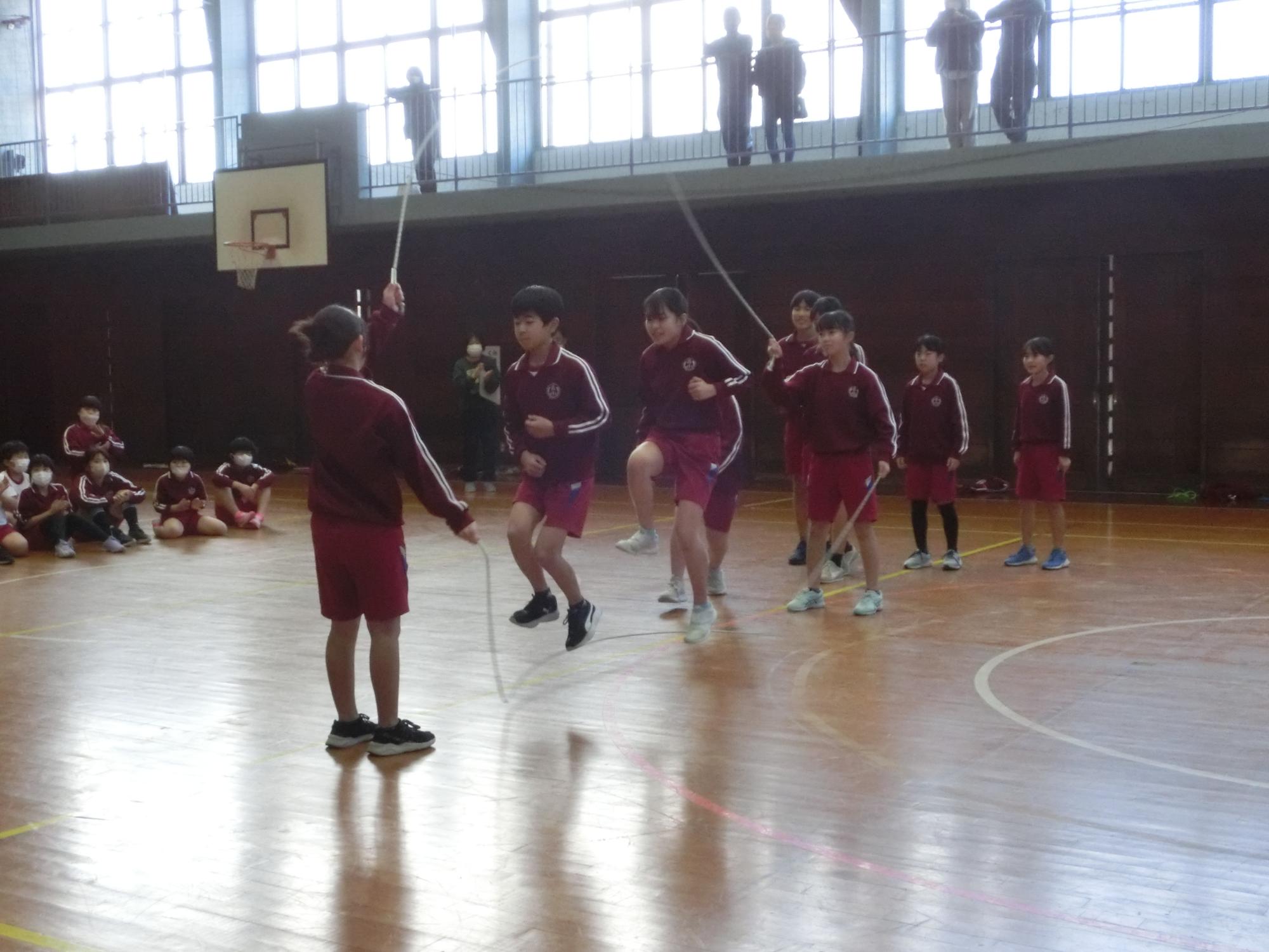 体育館で児童たちが大縄跳びに挑戦している写真