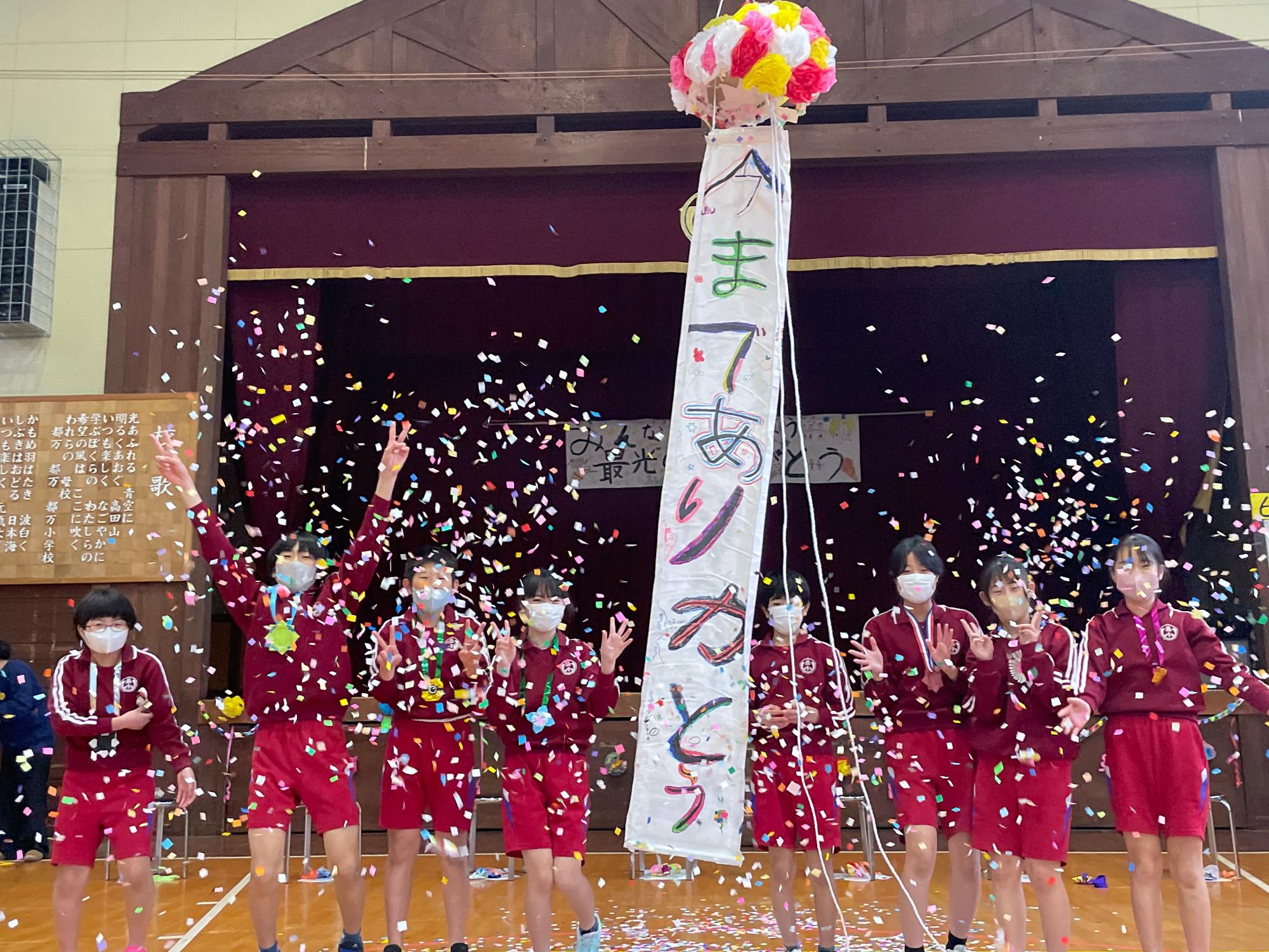 体育館で児童たちがくす玉を割ってお祝いしている写真