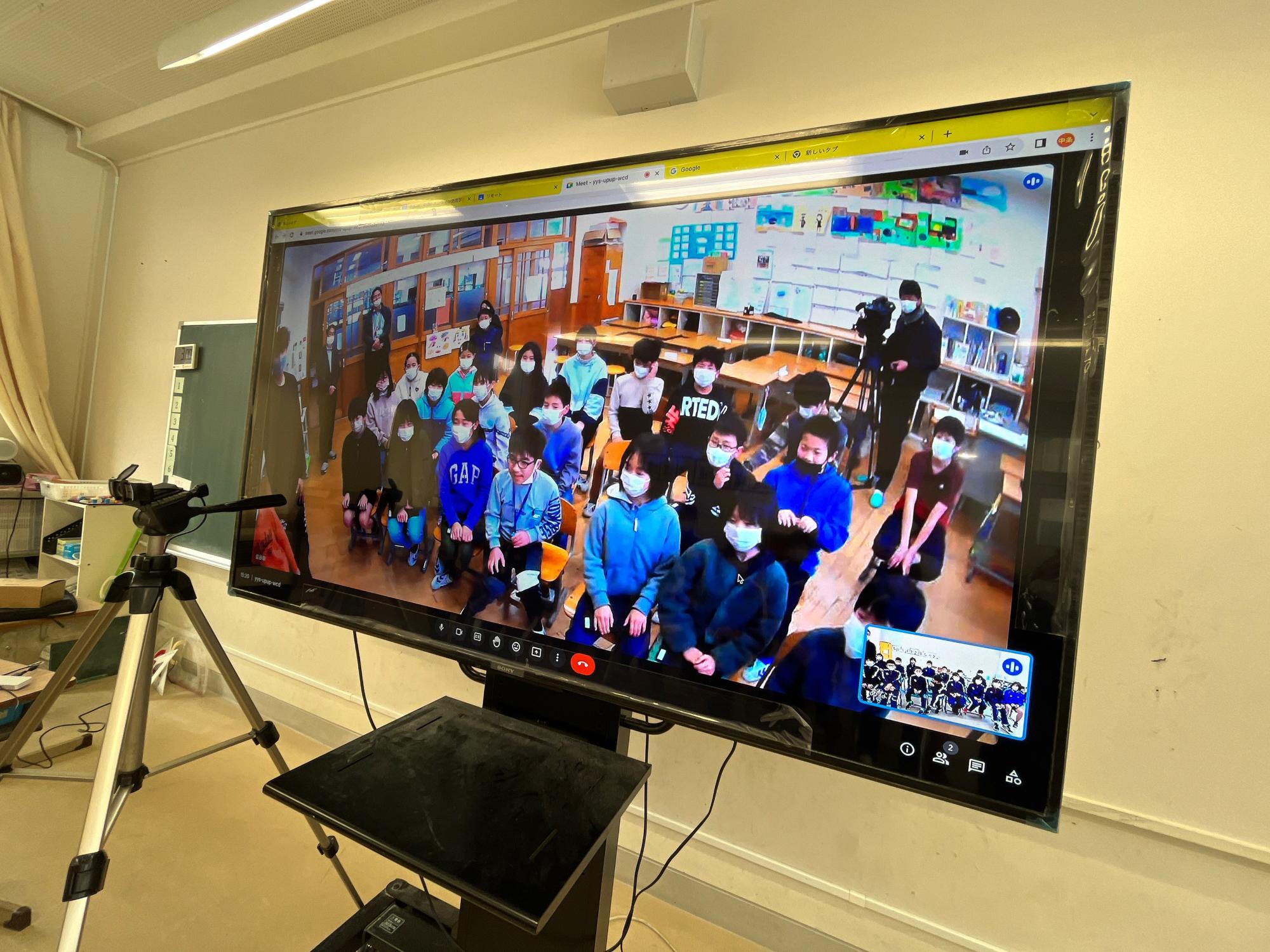 大勢の生徒が教室にいる様子が大きなモニターに映し出されている写真