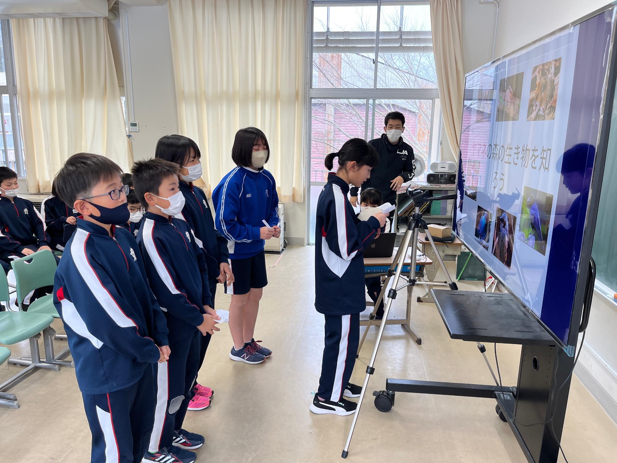 大きなモニターの前に女子児童が立っている写真