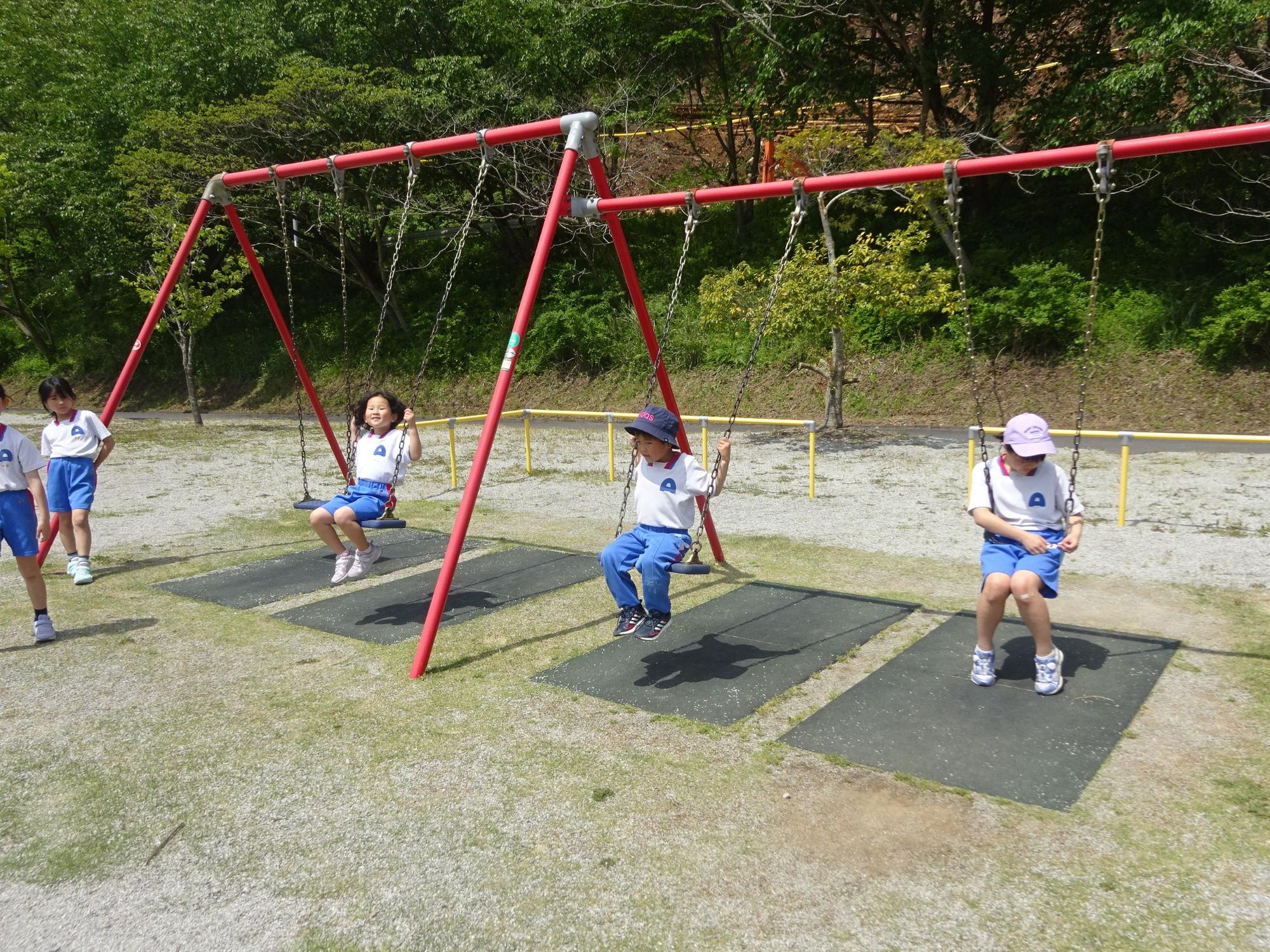 公園で体操着を着た児童がブランコで遊んでいる写真