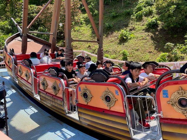 遊園地のアトラクションで児童たちが海賊船型の乗り物に乗っている写真