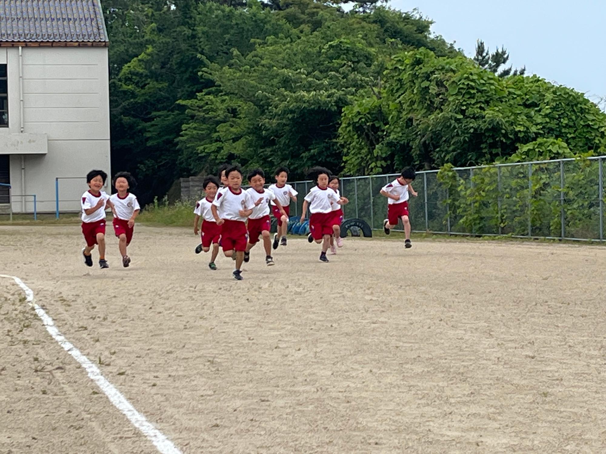 校庭で赤い体操着を着た児童たちが走っている写真
