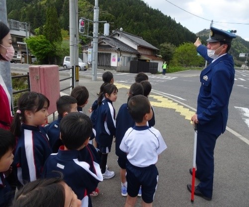 歩道を歩く児童たちを交通安全指導員と先生が見守っている写真