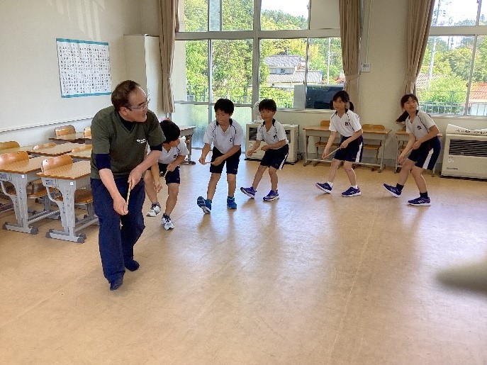 教室で一列に並び大人が児童たちに舞を教えている写真