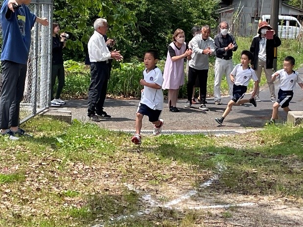 保護者に見守られながらマラソン大会を走っている児童たちを正面から見た写真