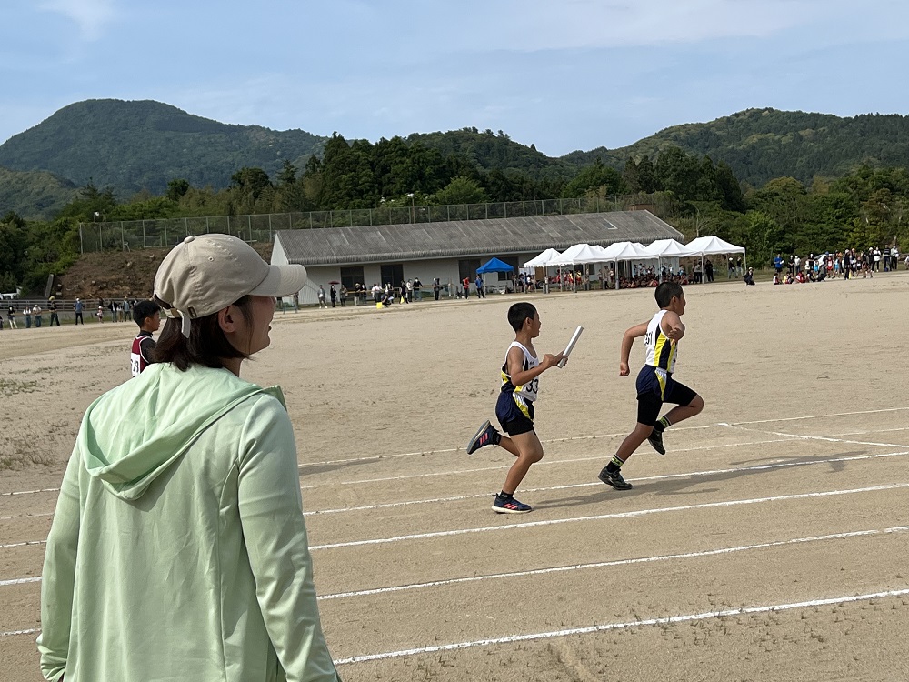 グラウンドでバトンを受け渡しながらトラックを走る児童たちの写真