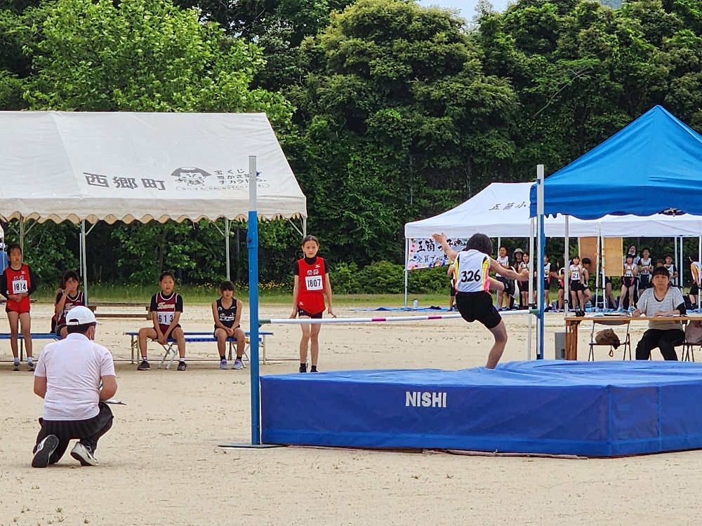 グラウンドの跳躍台で児童が走り高跳びに挑戦している写真