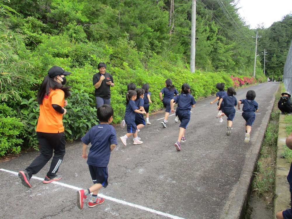 丘の道で2人の教師に見守られながら走り出す児童たちの写真