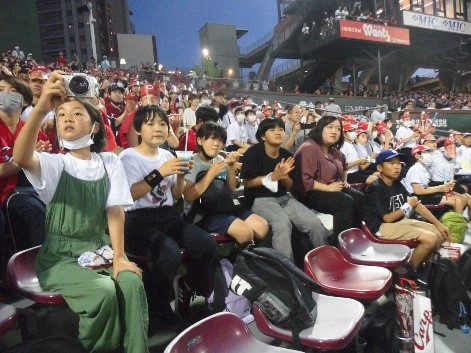 野球場の観客席で着席して試合を応援する児童たちの写真
