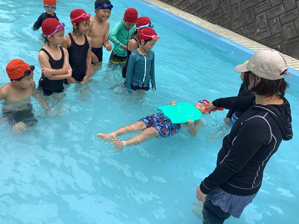 プールの中で先生に支えられながら浮きの練習をする児童たちの写真