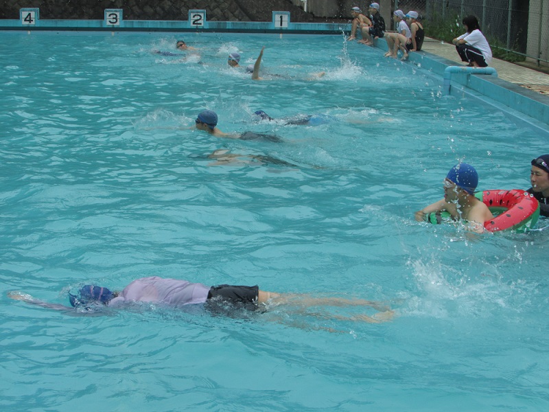 学校のプールで浮き輪などを使い泳ぎの練習に取り組む児童たちの写真