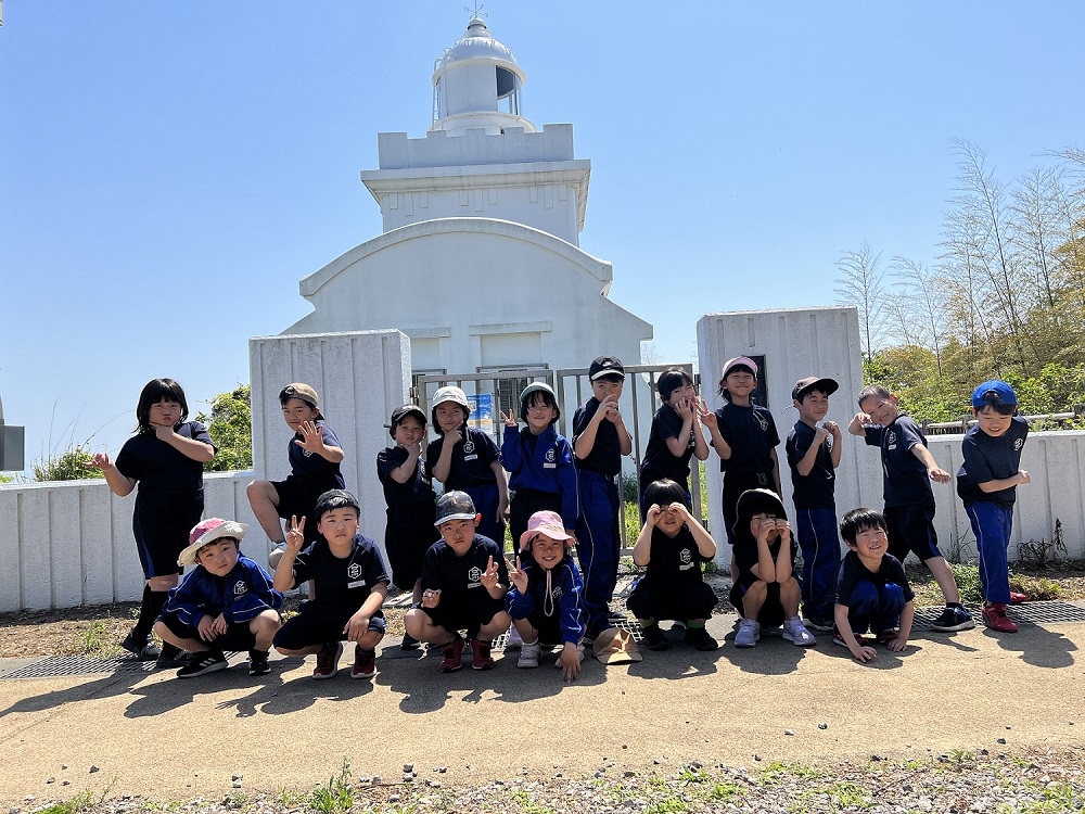 屋外の白い灯台の前でポーズをとる児童たちの集合写真