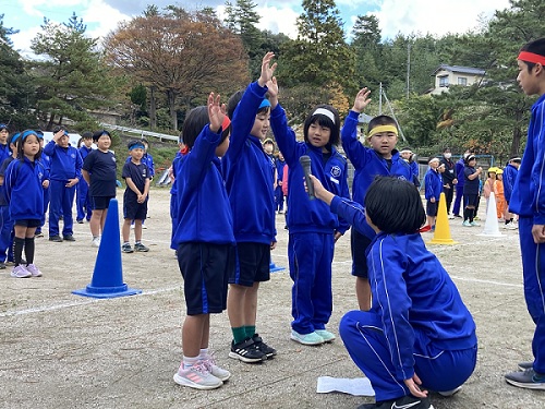 校庭で青い体操服を着た児童たちが選手宣誓をしている写真