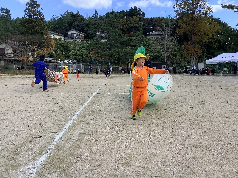 校庭でオレンジ色ののジャージを着た児童がグラウンドを走り回っている写真