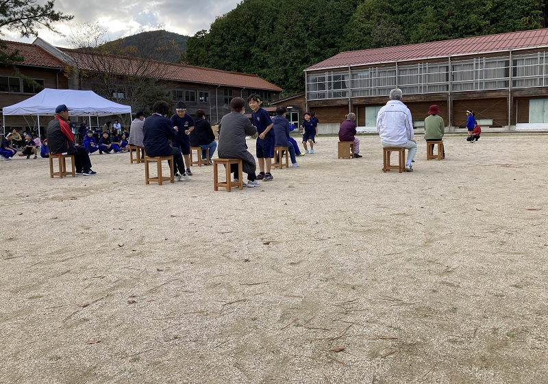 校庭で児童と地域の人たちが椅子取りゲームのような競技を楽しんでいる様子の写真