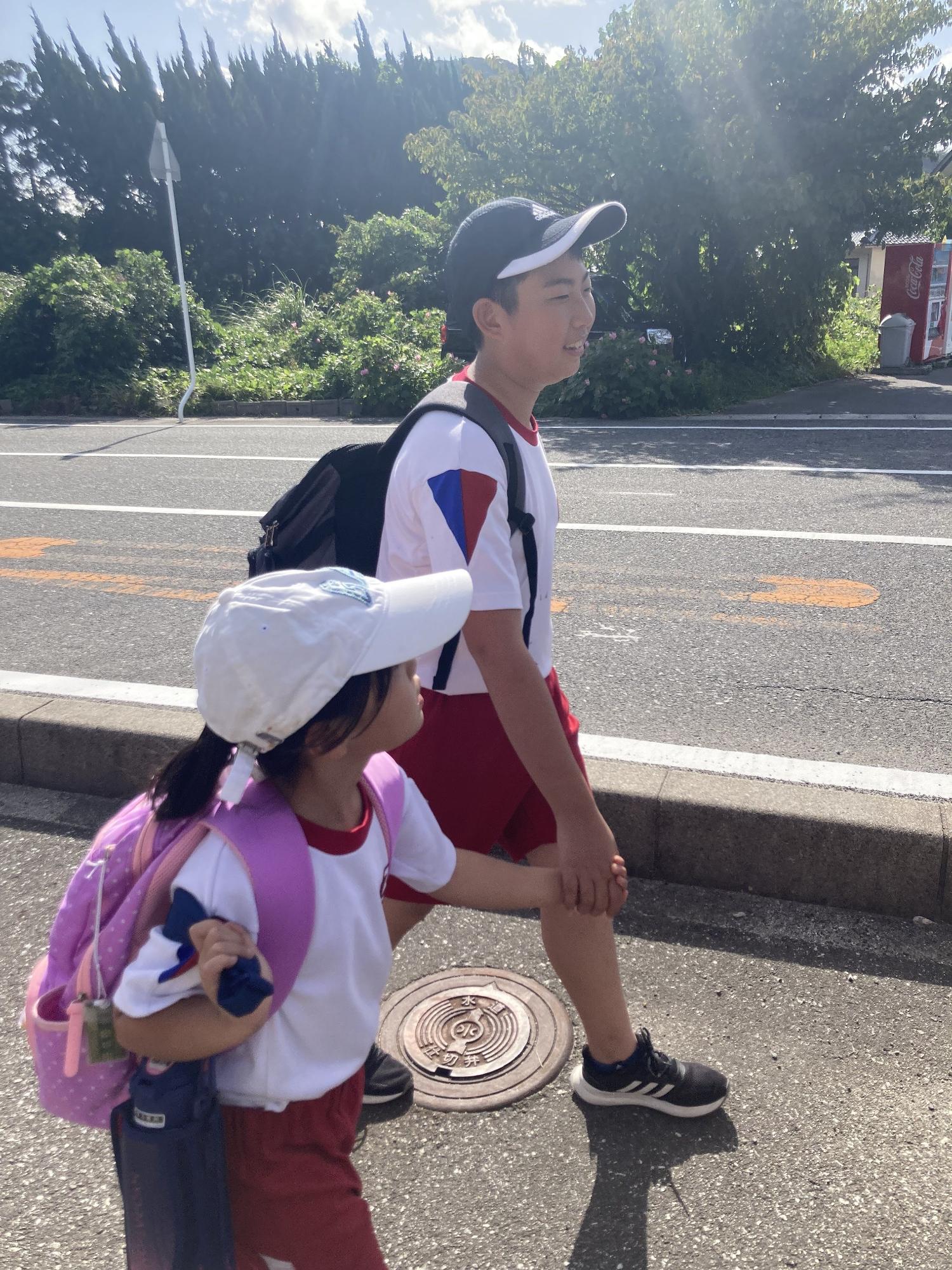 高学年の男子児童と低学年の女子児童が手をつないで歩いている写真