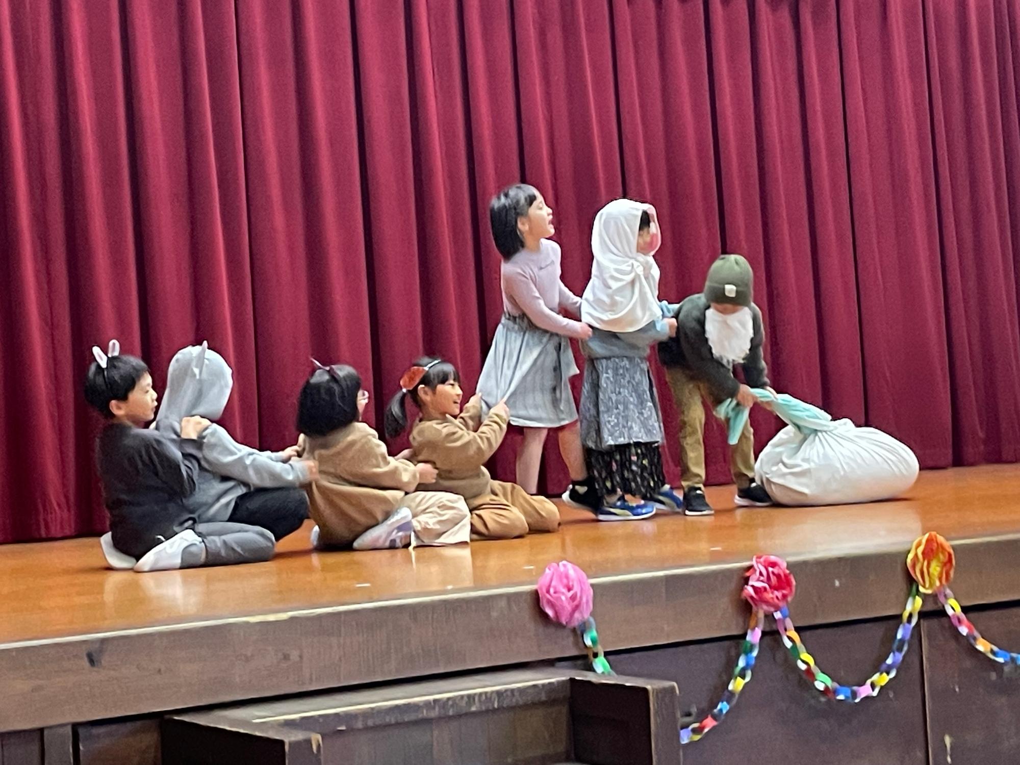 ステージで低学年の児童たちが衣裳を着て劇を演じている写真