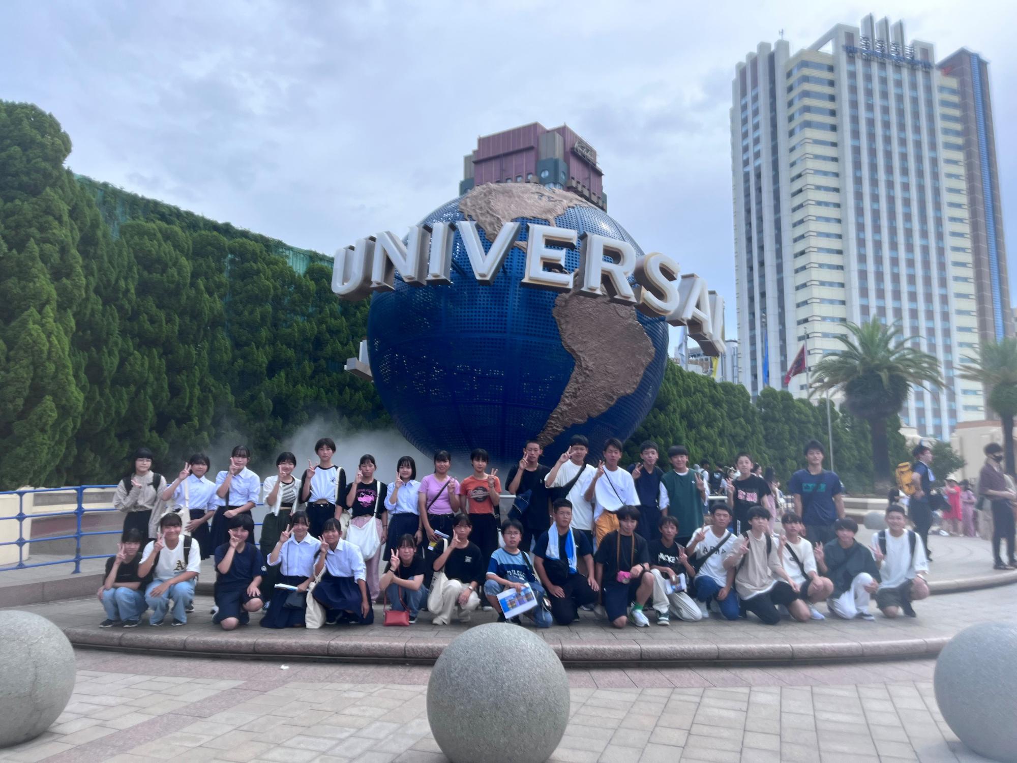 テーマパークの地球儀モニュメント前で、生徒たちが集合して記念撮影をしている写真
