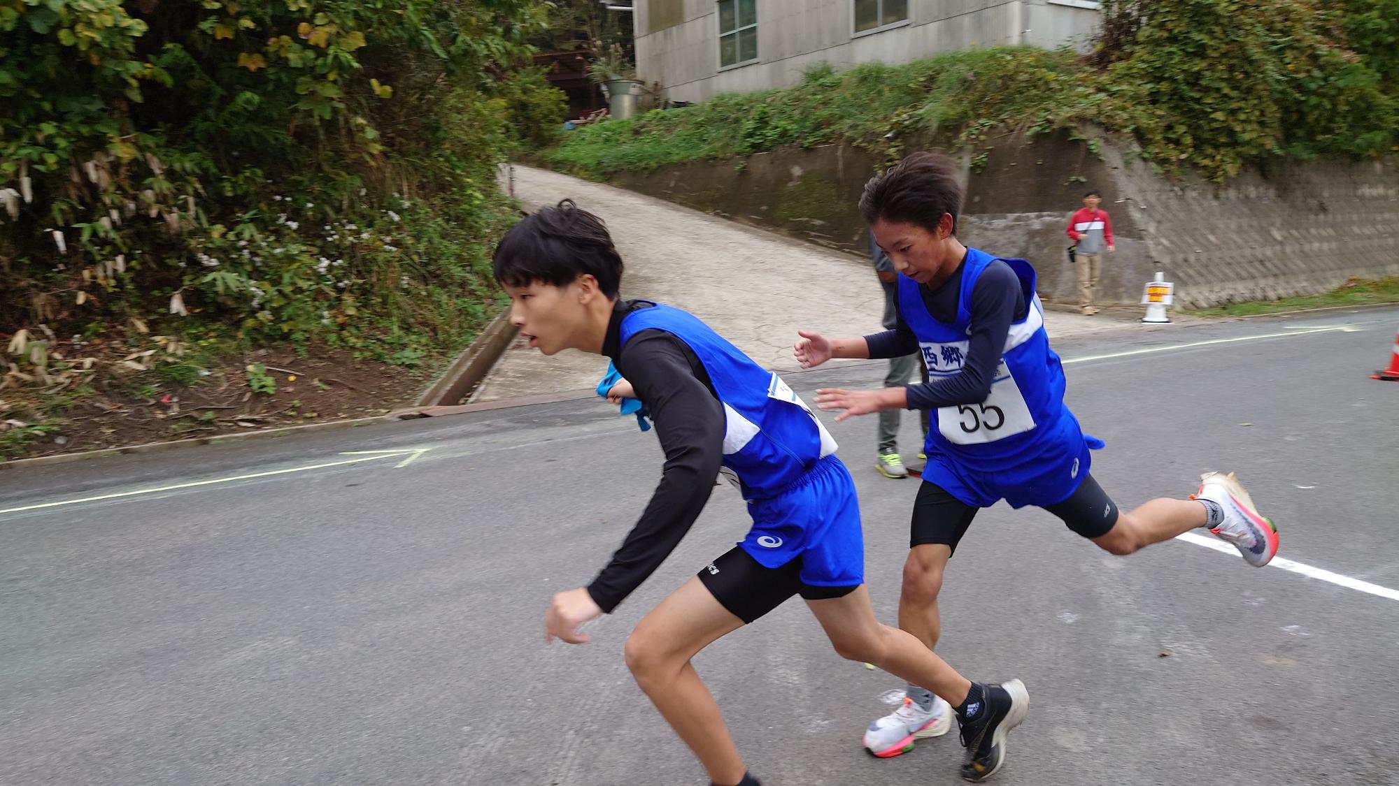 道路上で男子生徒がたすきを次の走者に渡している写真