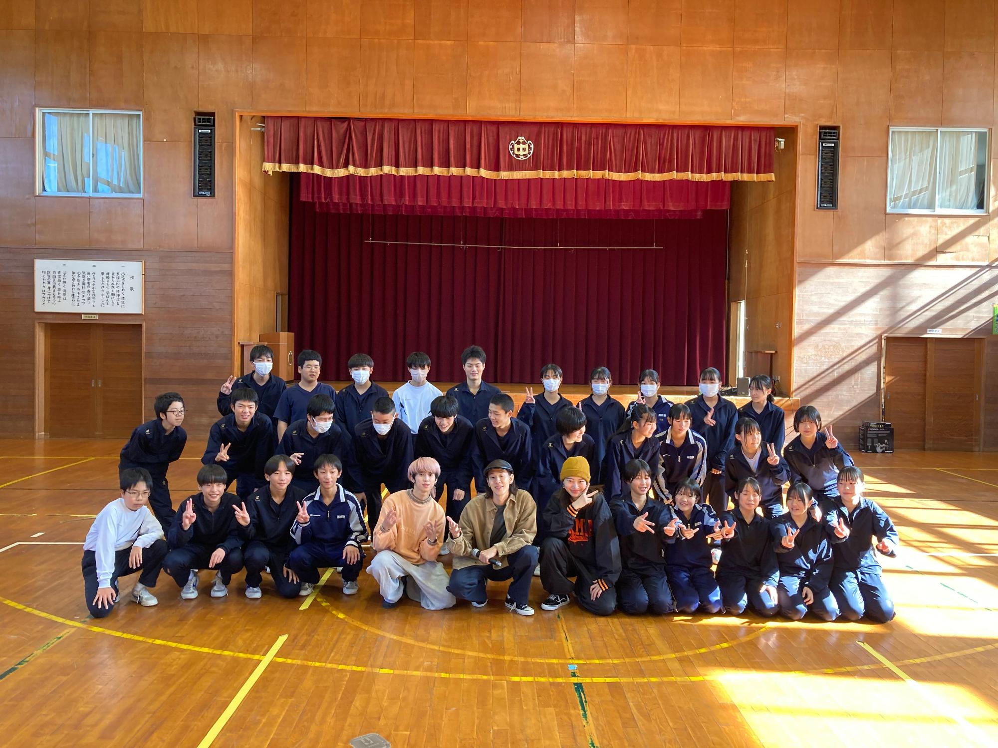 体育館の舞台前で生徒たちが集合して記念撮影をしている写真