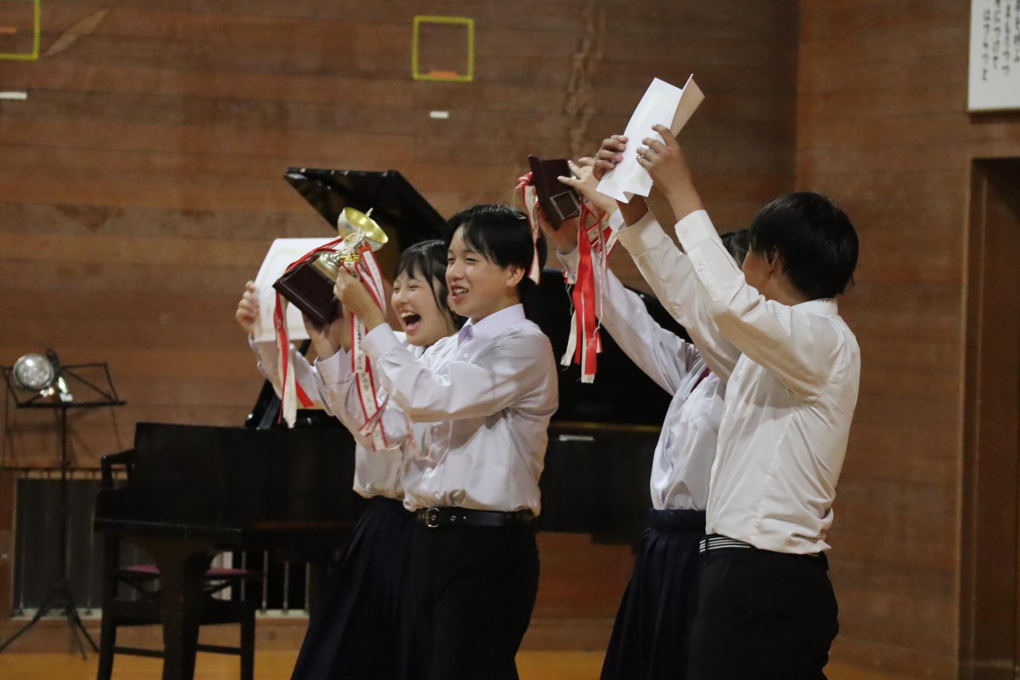 体育館で表彰状とトロフィーを掲げて喜ぶ生徒たちの写真